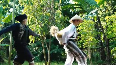 Bereketli yeşil bir çevrede iki kişinin olduğu sakin bir açık hava sahnesi. Bir kişi yerde oturuyor, siyah giyinmiş, diğeri ise arka planda, derin düşüncelere dalmış bir şekilde.. 