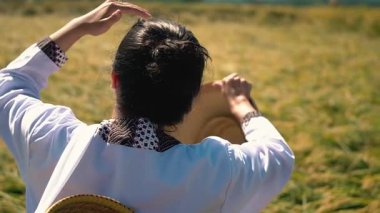 Geleneksel bir konik şapka giyen bir kişi pirinç tarlasında duruyor, sırtı kameraya dönük, yemyeşil alana doğru hareket ediyor. Sahne, kırsal yaşamın ve tarımın özünü yakalıyor..