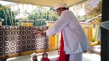 Geleneksel giyinmiş bir insan dekore edilmiş bir yerde kültürel bir ayin yapar. Ayar canlı renkler ve karmaşık desenler içeriyor, bitkiler ve sunumlar mevcut..