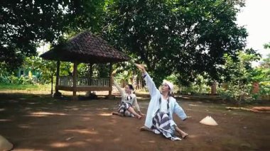 Bereketli yeşil bir çevrede iki kişinin olduğu sakin bir açık hava sahnesi. Bir kişi yerde oturuyor, siyah giyinmiş, diğeri ise arka planda, derin düşüncelere dalmış bir şekilde.. 