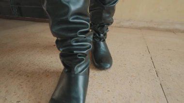 Pürüzlü tasarımı olan şık siyah lastik botların yakın çekimi, desenli bir zeminde duruyor. Odaklandıkları konu botlar. Eşsiz tarzlarını ve malzemelerini sergiliyorlar..