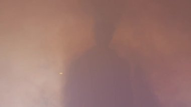 Sisli bir ortamda duran gizemli bir insan silueti. Yumuşak ışık, ruhani bir atmosfer yaratıyor..