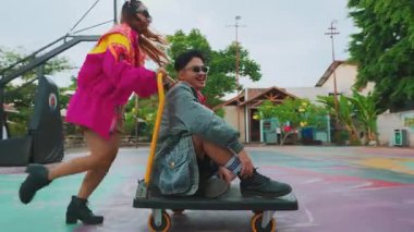 Açık hava basketbol sahasında bir bankta oturan genç bir adam, arka planda bir çemberle. Sarayda renkli sanat eserleri sergileniyor ve etrafı ağaçlar ve binalarla çevrili..