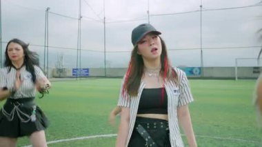 Spor sahasında şık kıyafetler giymiş iki dansçının olduğu dinamik bir sahne. Bir dansçı ön planda, enerjik bir şekilde kendinden emin bir ifadeyle performans sergiliyor, diğer dansçı ise biraz geride, canlı bir atmosfer ekliyor.