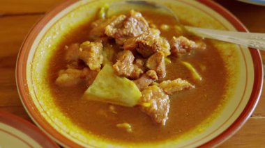 Tahta bir masada servis edilen lezzetli soslu taze et ve sebzeli bir kase baharatlı köri..