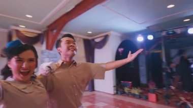 Kırsal bir salda çiftlerin neşeyle dans ettiği canlı bir dans sahnesi. Dekorasyonda ahşap kirişler, avizeler ve eski moda kıyafetler giyen katılımcılarla dolu kareli bir zemin yer alıyor..