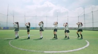 Bulutlu bir gökyüzünün altında çimenli bir alanda gösteri yapan altı dansçıdan oluşan bir grup. Şık kıyafetler giyiyorlar, enerjik dans figürleri sergiliyorlar. Sahne canlı ve dinamik bir atmosfer yakalıyor..