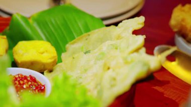 Taze sebzeler ve ahşap bir masada soslarla servis edilen, çıtır çıtır kızarmış atıştırmalıkların yer aldığı geleneksel Endonezya yemeğinin yakın çekimi..