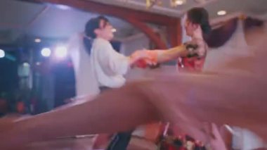 Diğer dansçılarla çevrili geleneksel kıyafetli bir çiftin dans gösterisi. Sahne, bir avize ve renkli kostümlerle hareket ve neşe yakalar..