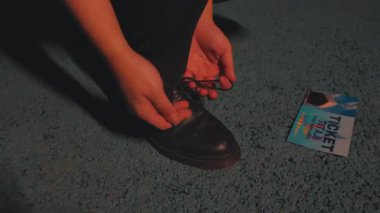 Ayakkabı bağcıklarını siyah bir ayakkabıya bağlayan ve biletini yakındaki dokulu mavi bir yüzeye koyan biri..