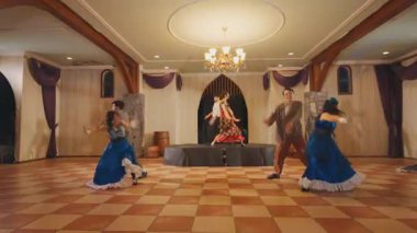 Sahnede renkli kostümler içinde altı dansçının olduğu canlı bir dans gösterisi. Dekor, avize ve ahşap aksanlı zarif bir dekor içeriyor ve şenlikli bir atmosfer yaratıyor..