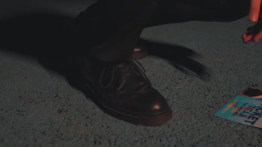 Bir insanın siyah ayakkabısının yakın plan resmi desenli bir yüzey üzerinde, yanında da bir bilet var. Ayakkabı boyalı ve bilet renkli. Bu da sıradan ya da olaylı bir ortam olduğunu gösteriyor..