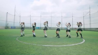 Altı dansçıdan oluşan dinamik bir grup, bulanık hareket etkisine sahip bir spor sahasında enerjik bir performans sergiliyorlar. Şık kıyafetler giyip bulutlu bir gökyüzünün altında canlı bir atmosfer sunuyorlar..