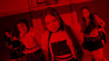 Çizgili elbiseli dansçıların olduğu bir spor salonunda dinamik bir dans gösterisi. Sahne kırmızı ışıkla aydınlatılıyor ve dramatik bir atmosfer yaratıyor. Dansçılar, enerjilerini ve koreografilerini sergileyerek hareket halindeler..