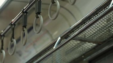 Metalik ve plastik elementlerin sergilendiği bir metro treninde asılı duran ellerin yakın çekimi. İç mekan, modern bir şehir geçiş ortamını yansıtıyor..