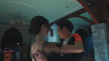 Işıl ışıl bir ortamda iki kişinin yakından dans edişinin yakın çekimi. Bir kişi siyah bir takım giyerken, diğeri şık bir elbise giyiyor. Atmosfer samimi ve zarif, yumuşak ışıklandırmalı..