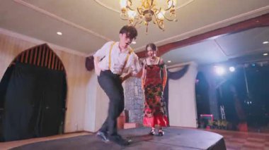 Zarif bir balo salonunda dans eden bir çift. Erkek pantolon askısı olan beyaz bir gömlek giyer, kadın ise renkli, çiçekli bir elbise giyer. Yukarıdaki avize sahneye biraz cazibe katıyor..