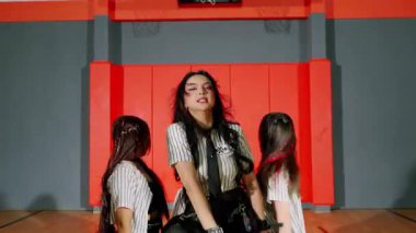 Dinamik bir dans gösterisi. Siyah etekli, çizgili tişörtlü, şık bir bayan dansçının basketbol kortunda arka planda dans etmesi..