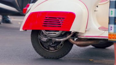 Antika bir scooter 'ın arka tekerlek ve motorunun yakın çekimi, eşsiz tasarımı ve canlı renkleri sergiliyor. Scooter, ayrıntılı ayrıntılarıyla kırmızı ve beyaz bir renk şemasına sahiptir..
