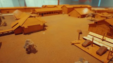 Tarihi bir köyün detaylı bir modeli, ahşap yapılar ve binalar bir düzen içinde sergileniyor. Sahne kumlu bir zeminde geçiyor. Minyatür evlerin ve manzaraların işçiliğine odaklanıyor..