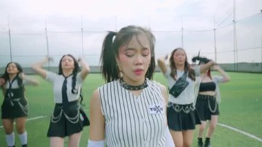 Bir grup genç kadın bir spor sahasında dans gösterisi yapıyor. Onlar şık kıyafetler giyiyorlar. Sportif ve stresli bir modaya sahipler. Sahne canlı ve enerjik, bir koreografi anı yakalıyor..