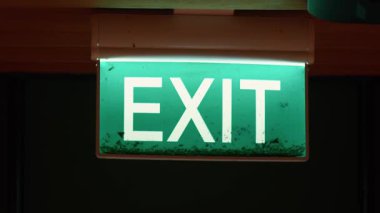 Koyu beyaz harflerle 'EXIT' kelimesinin gösterildiği yeşil bir çıkış işareti yakıldı. İşaret biraz tozlu, yakın zamanda temizlenmemiş olabilir..