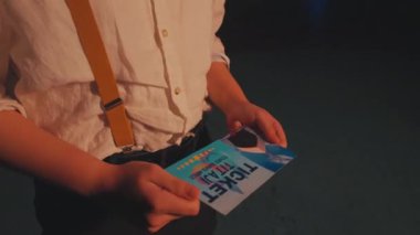 Pantolon askısı olan beyaz bir gömlek giyen biri, düşük ışık ayarında yakalanmış. Arka plan bulanık, hareket ya da canlı bir atmosfer olduğunu gösteriyor..