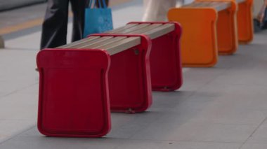 Halka açık bir alanda kırmızı ve turuncu tasarımların yer aldığı renkli banklar, insanların yakınlarda yürüdüğü. Banklar modern ve işlevseldir, temiz bir şehir zeminine karşıdır..