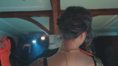 Zarif bir ortamda yakın dans eden bir çift romantik bir atmosfer sergiliyor. Kadın göz alıcı bir elbise ve turuncu eldivenler giyer, erkek ise resmi giyinir. Yumuşak ışıklandırma havayı geliştirir..