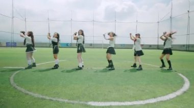 Parlak gökyüzünün altındaki bir spor sahasında altı dansçıdan oluşan bir grup. Şık kıyafetler giyiyorlar, dinamik pozlar veriyorlar, koreografilerini sergiliyorlar..