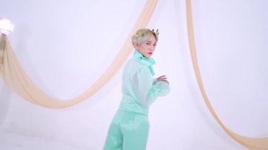 Nane yeşili kıyafetli şık bir şahıs, akıcı kumaşlı minimalist bir arkaplana karşı poz veriyor. Sahne parlak ve modern, moda ve zarafeti vurguluyor..