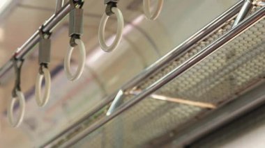 Metal korkulukların ve metro treninin içinde asılı halkaların yakın çekimi modern bir şehir ulaşımı ortamı sergiliyor..