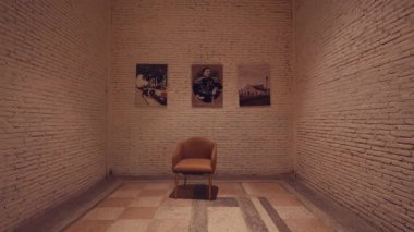 Ortasında tek bir sandalye bulunan minimalist bir galeri. Üç çerçeveli fotoğraf beyaz tuğla duvarda asılı, sakin ve düşünceli bir atmosfer yaratıyor..