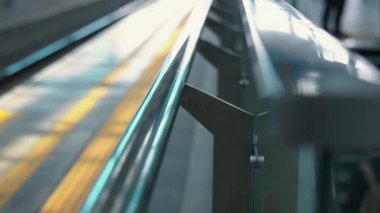 Arka planda bir çocuğun yürüdüğü, modern bir ortamda parmaklıkların bulanık görüntüsü. Odak noktası, yerdeki sarı çizgilerle parlayan metal korkuluklar..