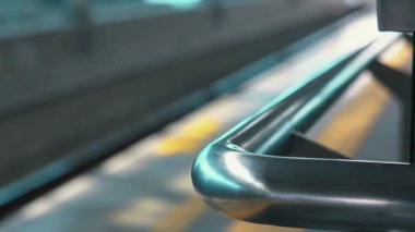 Bir tren istasyonundaki metalik tırabzanın yakın plan görüntüsü. Arka planda bulanık izler var. Görüntü, modern mimariyi vurgulayarak demiryolunun yüzeyindeki parlak tasarım ve yansımaları yakalıyor..