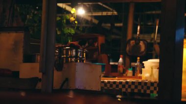 Kareli bir masanın üzerinde çeşitli mutfak aletleri ve konteynırları olan loş bir mutfak sahnesi. Atmosfer, uzayı aydınlatan sıcak ışıkla sıcak ve sade..