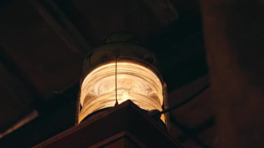 Ahşap bir kirişten asılı, yumuşak bir şekilde parlayan eski bir fener. Sıcak ışık, çevredeki kırsal cazibeyi vurgulayan rahat bir atmosfer yaratıyor..