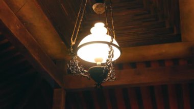 Ahşap tavandan sarkan, sıcak bir ışıkla aydınlatılmış klasik bir avize. Avize karmaşık bir metal işçiliği ve klasik bir tasarım içeriyor..