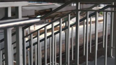 Tren istasyonunun bulanık arka planına sahip metal bir merdiven korkuluğunun yakın görüntüsü. Odak noktası geometrik çizgiler ve parmaklıkların yapısı, modern bir estetik yaratıyor..