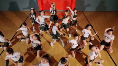 Enerjik bir koreografinin sergilendiği bir spor salonunda canlı bir dans grubu. Dansçılar aynı kıyafetleri giyerler, beyaz bluzlar ve siyah etekler giyerler, dinamik bir düzenle.