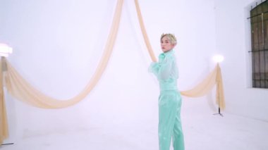 Minimalist stüdyo ortamında beyaz bir arka plan ve yumuşak kumaşla poz veren bir model. Modern moda estetiğini sergilemek için zarif, yeşil bir elbise giyiyorlar..