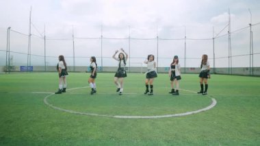 Bir futbol sahasında dans eden altı kız grubu. Kareografik bir düzende dizilmişler. Bulutlu bir gökyüzünün arka planına karşı senkronize hareketlerini sergiliyorlar..