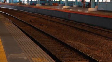 Demiryolu rayları olan bulanık bir geçmişi ve raylara odaklanmış bir tren istasyonu platformu. Platform boş, uzaktan görülebilen bir yer var..