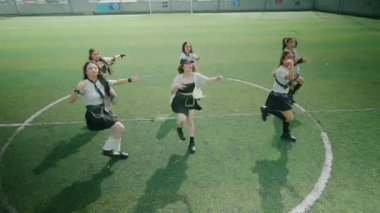 Yeşil bir futbol sahasında altı dansçıdan oluşan bir grup. Şık siyah beyaz kıyafetler giyiyorlar, senkronize dans figürleri sergiliyorlar. Sahne onların enerjilerini ve takım çalışmalarını yakalıyor..