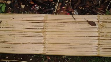 Ahşap bir yüzeye yakın çekim, çoklu paralel oyuklar, işçiliği gösteriyor. Etrafta bir el, bazı aletler ve doğal döküntülerle birlikte görülebilir..