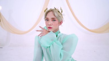 Açık yeşil giysili, uzun kollu, yapraklardan bir taç takmış bir adam. Arka plan yumuşak ve minimalistik, ruhani görünümü güçlendiriyor..