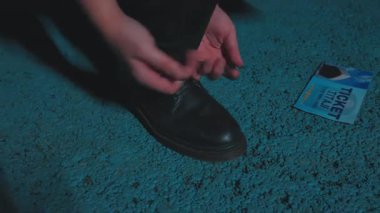 Dokulu bir yüzeye çömelmiş bir insan, bir bilet alıyor. Bilet kısmen görülebiliyor ve 'TICKET' kelimesi belirgin bir şekilde kullanılıyor. Sahnenin karamsar, loş bir atmosferi var..