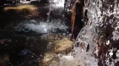 Su damlacıkları ve doğal çevresiyle kayaların üzerinden temiz bir havuza dökülen şelalenin yakın görüntüsü..