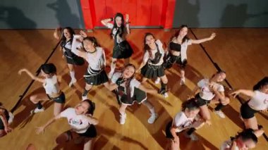 Dinamik bir amigo takımı basketbol sahasında koordineli bir gösteri yapıyor. Grup uyumlu kıyafetler giyiyor, enerjik pozlar ve ifadeler sergiliyor..