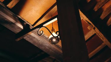 Kaliteli bir lamba ahşap tavandan sarkıyor ve sıcak bir parıltı bırakıyor. Kırsal ışınlar ve karanlık tonlar rahat bir atmosfer yaratıyor..